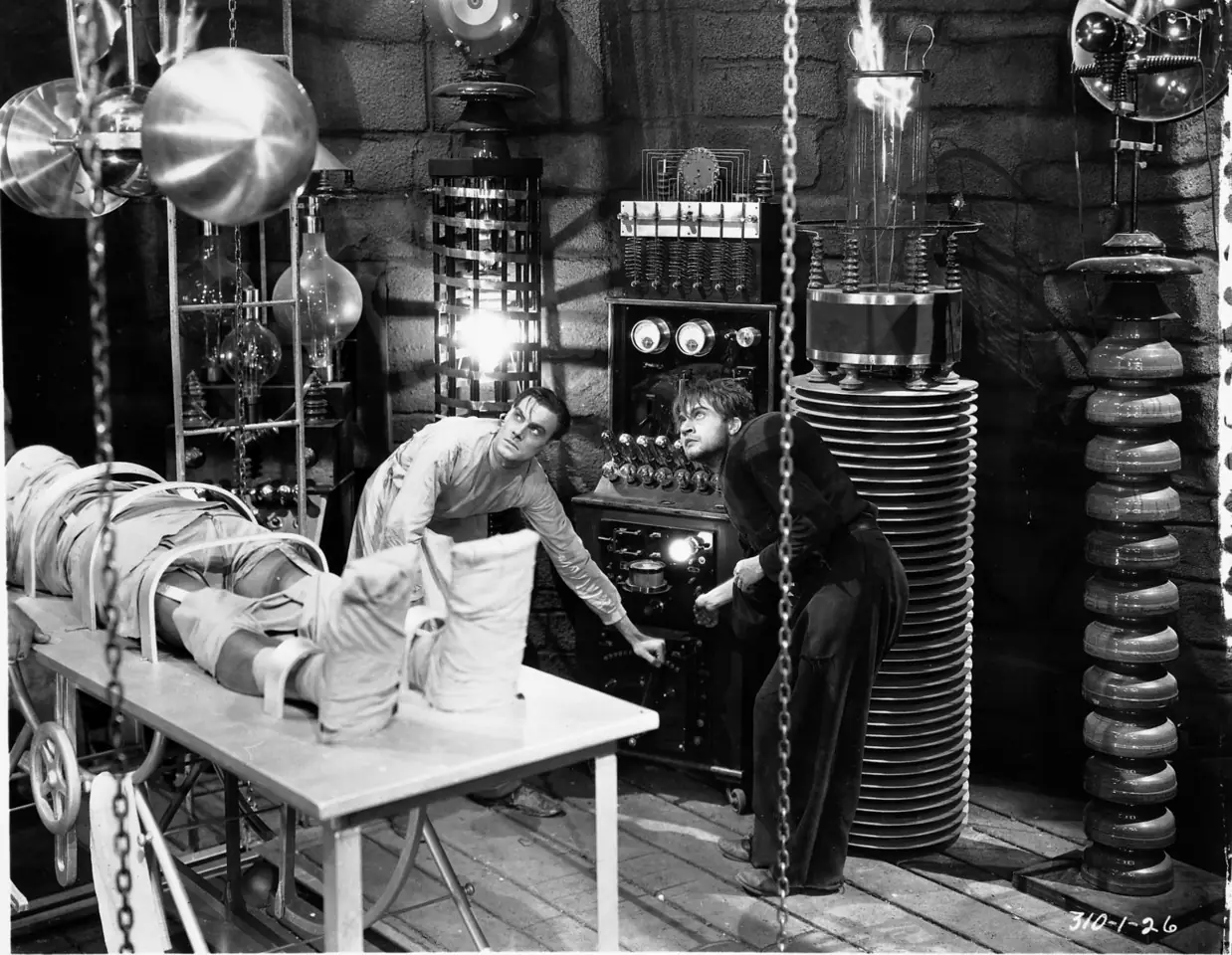 Scientists and electrical instruments in a classic black-and-white laboratory.